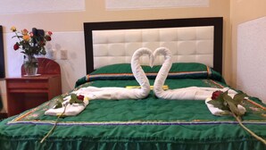 Cama com colcha verde e cabeceira branca. Há duas toalhas moldadas em formato de cisne sobre a cama.