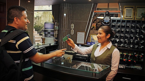 Uma área de recepção de hotel com balcão de vidro, uma máquina de café e um painel exibindo diversos objetos.