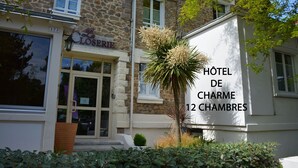 Een hotel genaamd "Hôtel de Charme" met een gevel van steen en een bord waarop "12 chambres" (12 kamers) staat.