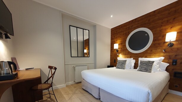 Hotelkamer met een groot bed, een bureau met waterkoker, een stoel, een ronde spiegel en een houten accentmuur.