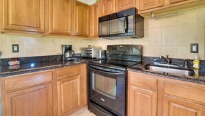 A kitchen with wooden cabinets, a black stove, a microwave, a sink, and a countertop with various appliances. - Quiet Davenport Home w/ Community Amenities! (Davenport)