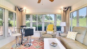 A spacious room with a large window, a ceiling fan, a beige sofa, a white armchair, a glass table, and a patterned rug. - Quiet Davenport Home w/ Community Amenities! (Davenport)