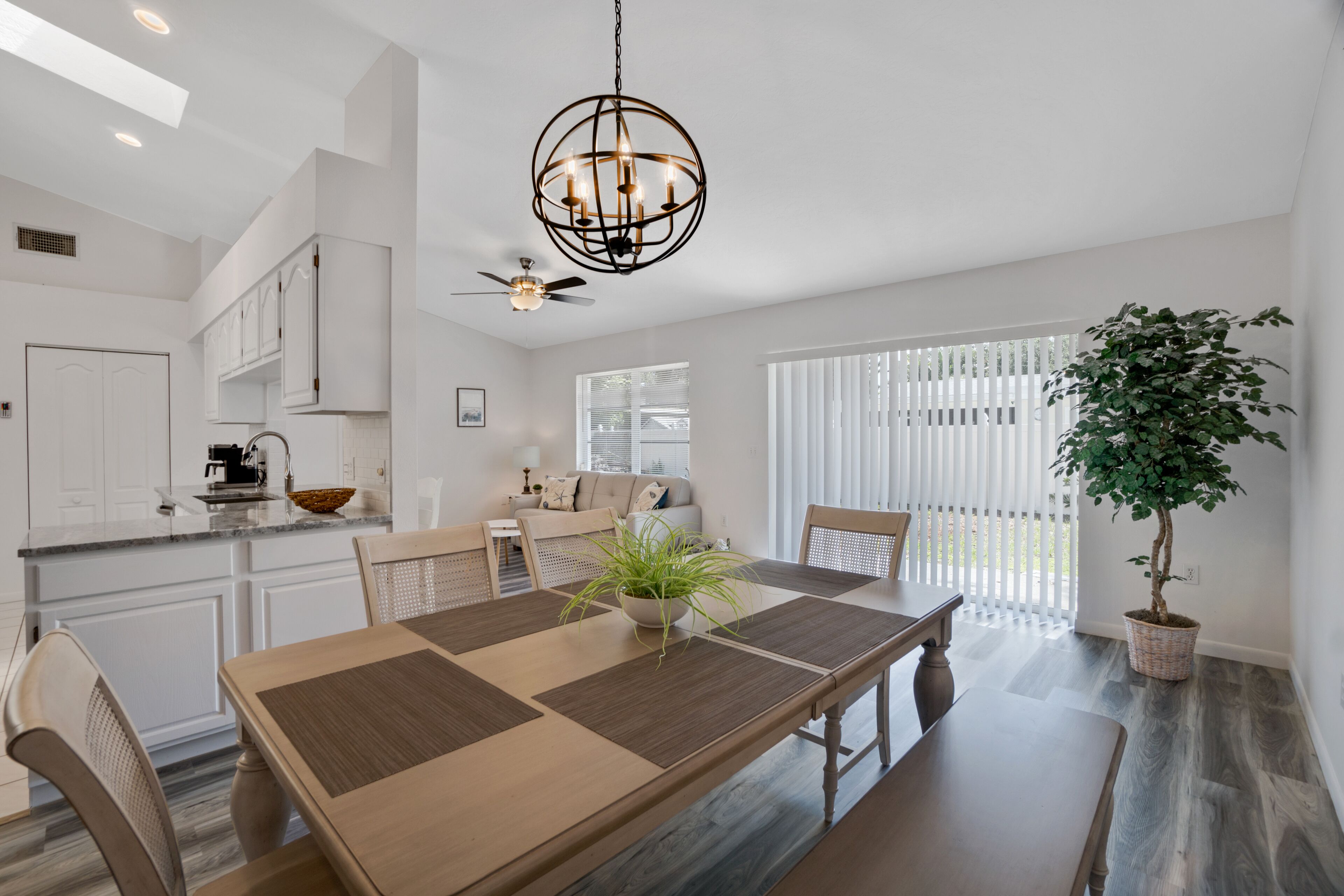 Une cuisine moderne avec des meubles blancs, un coin repas doté d’une table en bois et une plante en pot.
