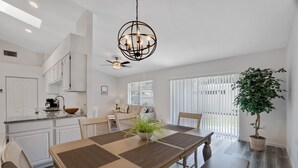 Eine moderne Küche mit weißen Schränken, einem Essbereich mit Holztisch und einem Blumentopf.