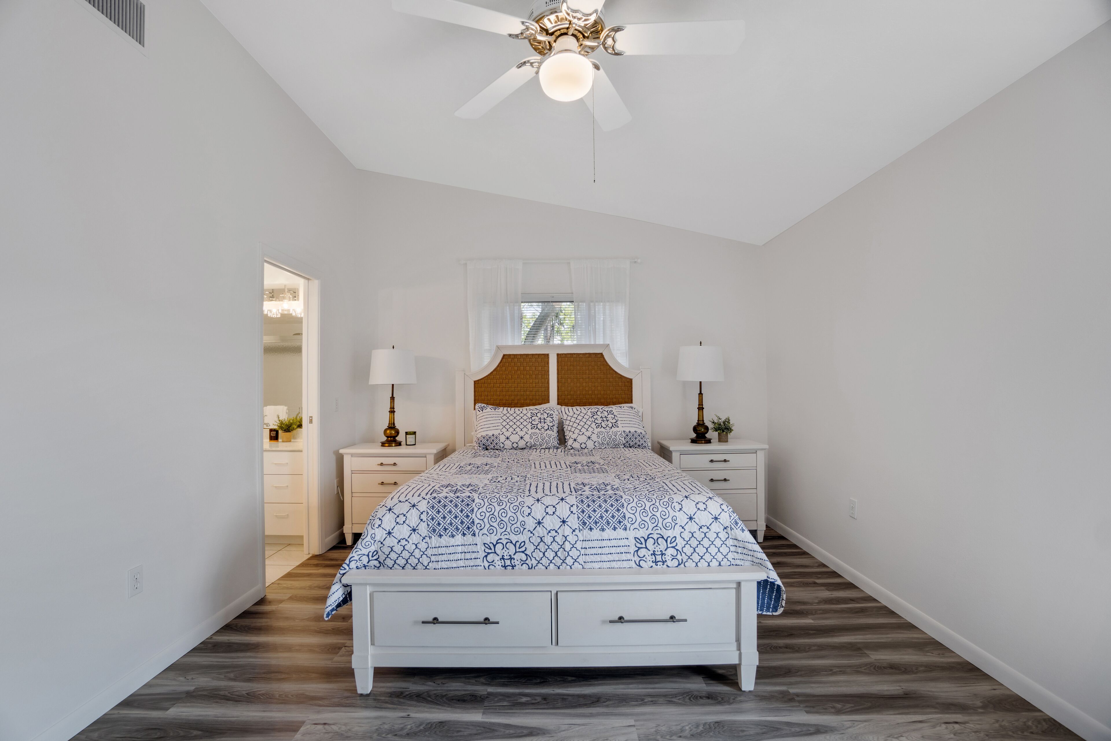 A bedroom with a bed, nightstands, a ceiling fan, and a window with curtains.