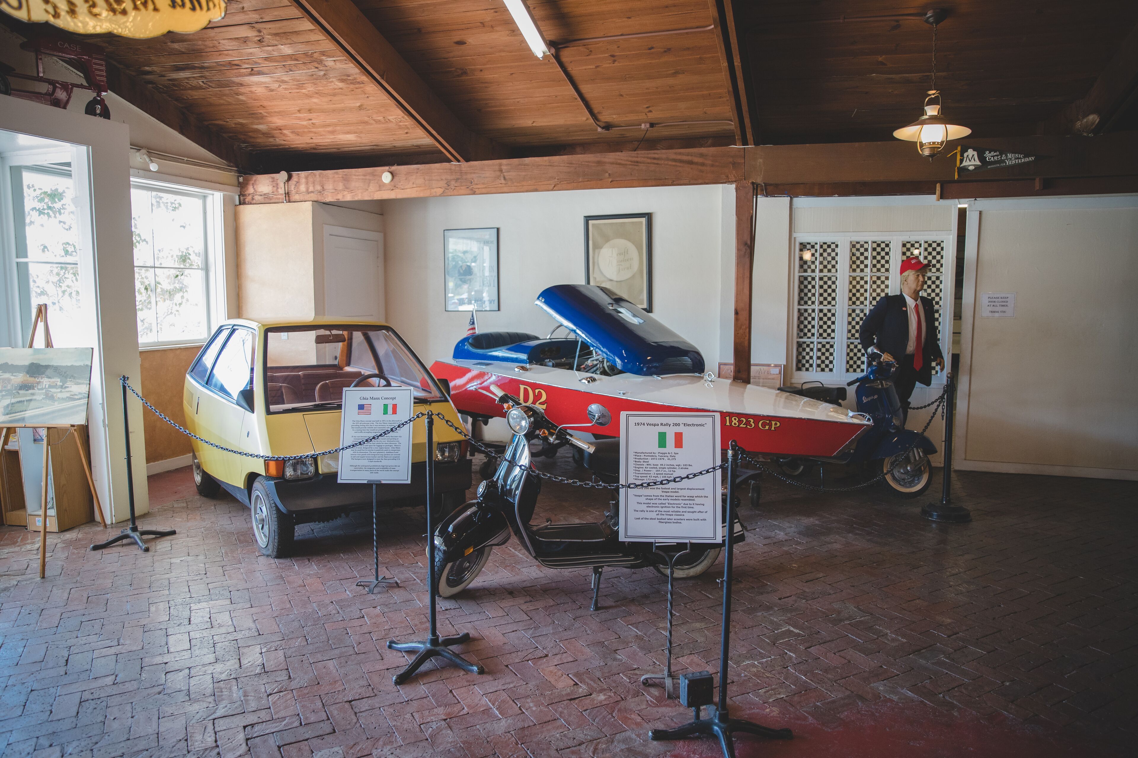 Un coche antiguo y una motocicleta expuestos, con carteles informativos y una barrera de cadena.