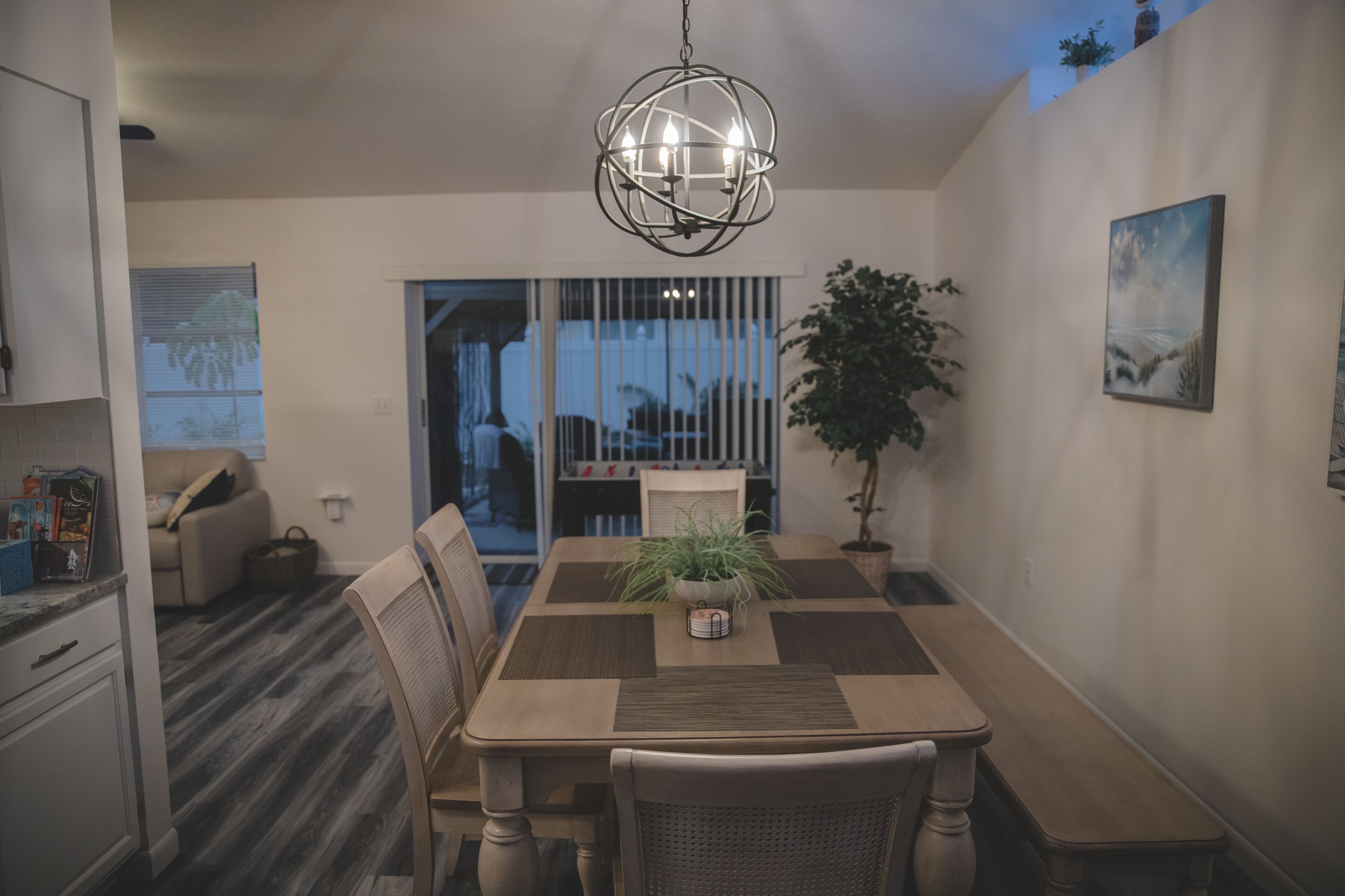 A dining area with a wooden table, chairs, a potted plant, and a hanging light fixture.
