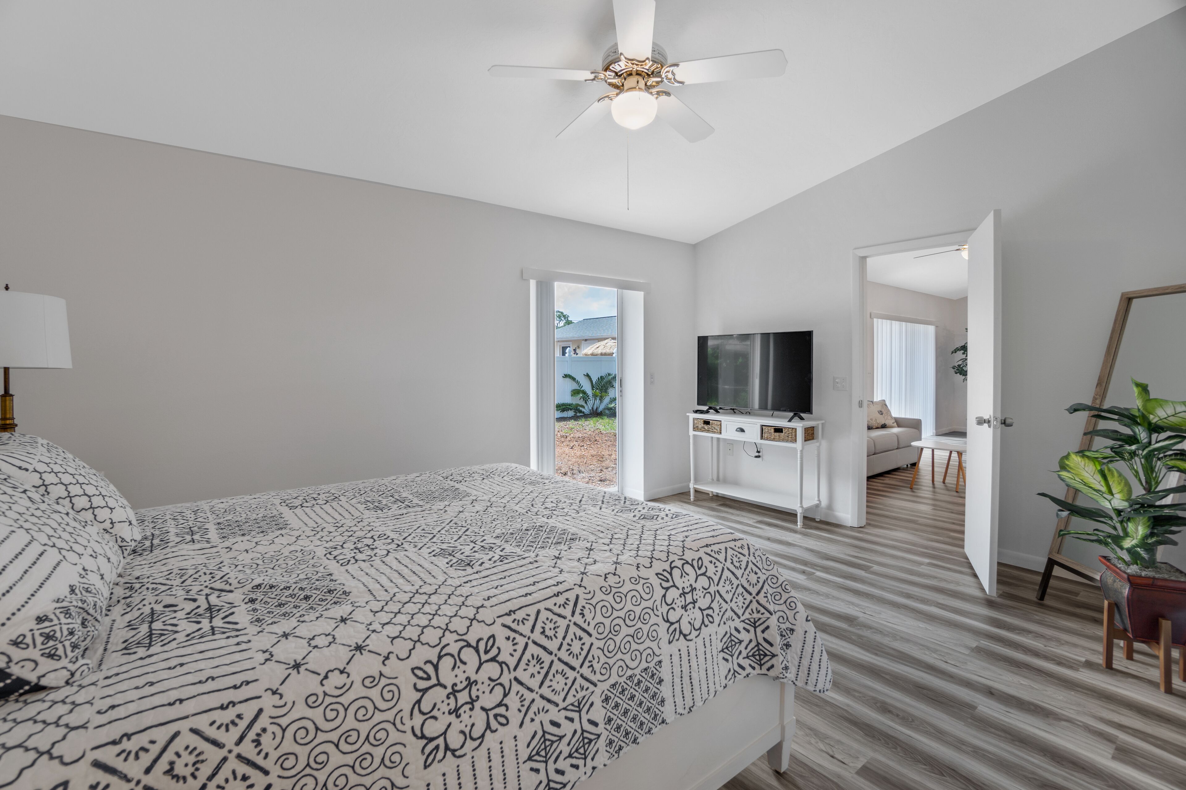 A bedroom with a bed, a ceiling fan, a TV, and a view of the outdoors.