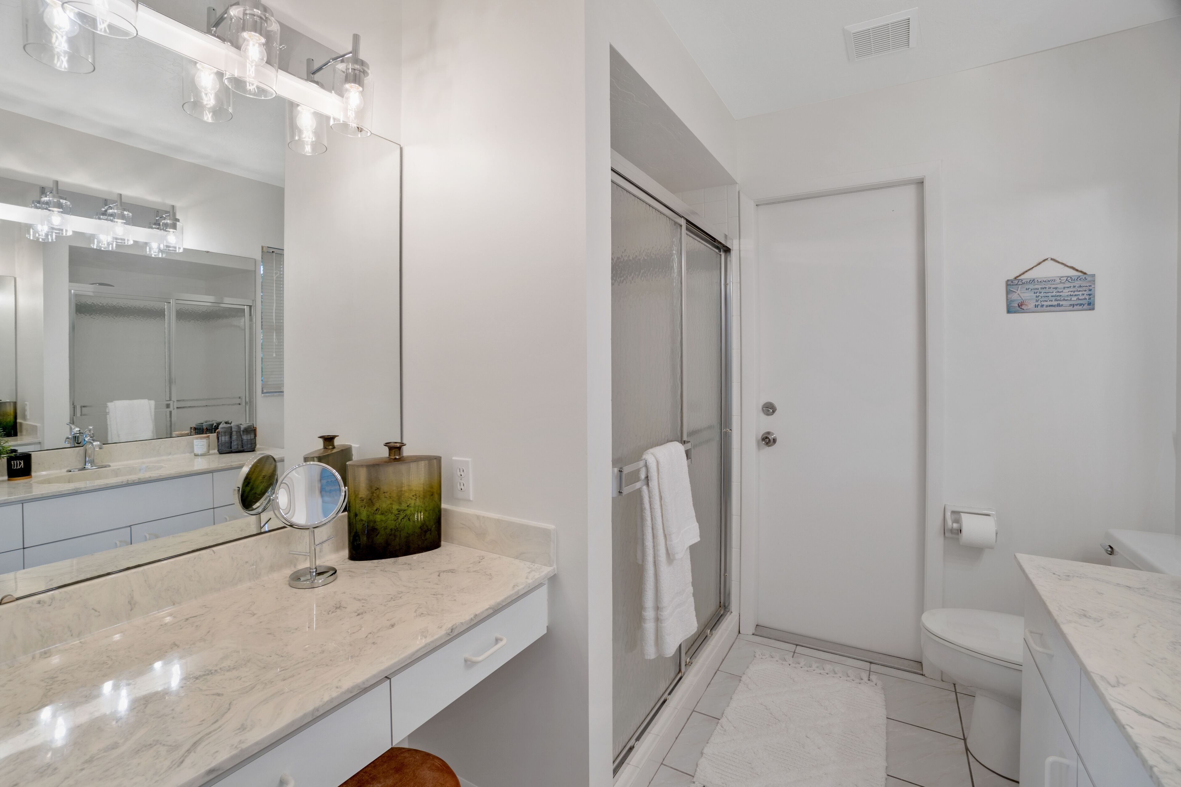 A modern bathroom with a marble vanity, a glass shower enclosure, and a white toilet.