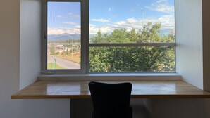 A room with a desk and a chair, a window with a view of a road and greenery, and a clear sky. - Stylish Downtown Loft 201-Alaska Railroad Suite (Anchorage)