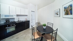 A modern kitchen with black cabinets, a gas stove, and a built-in oven. There is a dining table with four chairs and a potted plant. - Stylish Downtown Loft 201-Alaska Railroad Suite (Anchorage)