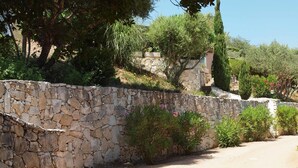 A stone wall with a dirt path leading through a garden with various plants and trees. - Les Chambres de Casarina (Bonifacio)