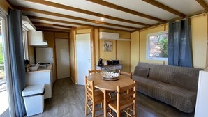 A compact living space with a kitchenette, a dining table with chairs, a sofa, and a window with curtains. - Les Chambres de Casarina (Bonifacio)
