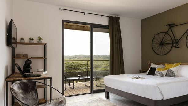 A bedroom with a bed, a desk with a laptop, a chair, a TV, and a balcony with a bicycle. - Les Chambres de Casarina (Bonifacio)