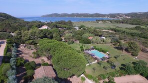 A residential area with a swimming pool surrounded by greenery, a clear view of the sea, and distant hills. - Les Chambres de Casarina (Bonifacio)