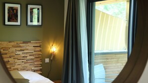 A bedroom with a wooden headboard, a bed with white bedding, a wall-mounted light, and a window with curtains. - Les Chambres de Casarina (Bonifacio)