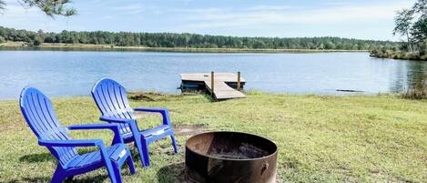 Un cadre idyllique au bord du lac, avec deux chaises Adirondack bleues, un foyer et une jetée en bois qui s’avance dans l’eau.