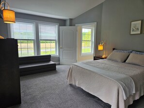 A bedroom with a bed, a nightstand, a lamp, a window, and a door.