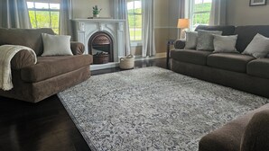 A living room with two sofas, a fireplace, a flat-screen TV, and a large window with curtains.
