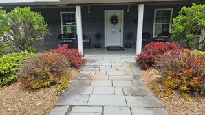 A house with a stone pathway leading to a front door, surrounded by various shrubs and plants.