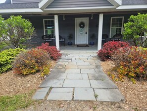 A house with a stone pathway leading to a front door, surrounded by various shrubs and plants.
