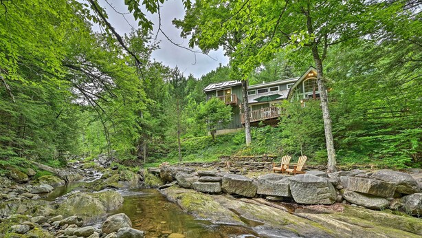 A cabin with a stone bridge over a stream, surrounded by dense forest. - Beautiful Jay Peak Home Near Creek & Waterfalls! (Jay)
