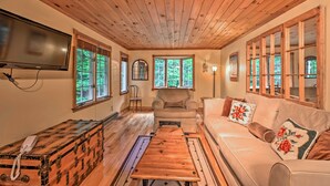 A cozy room with wooden ceiling, a sofa, a wooden table, and a vintage suitcase. - Beautiful Jay Peak Home Near Creek & Waterfalls! (Jay)