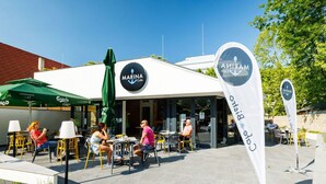 An outdoor seating area with tables and chairs, a green umbrella, and a sign for 'Marina Cafe'. - Nice apartment for 4 people with pool, WIFI, A/C, TV, terrace and pets allowed (Balatonfüred)