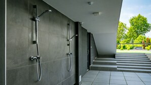 A modern bathroom with two showerheads, a visible ceiling-mounted security camera, and a staircase leading to an outdoor area with greenery. - Nice apartment for 4 people with pool, WIFI, A/C, TV, terrace and pets allowed (Balatonfüred)