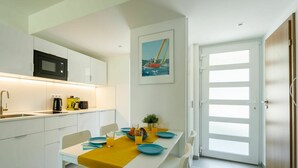 A modern kitchen with white cabinets, a black microwave, and a coffee maker. There is a dining table with blue plates and a yellow table runner. A painting of a sailboat is on the wall, and a door with frosted glass panels is visible. - Nice apartment for 4 people with pool, WIFI, A/C, TV, terrace and pets allowed (Balatonfüred)
