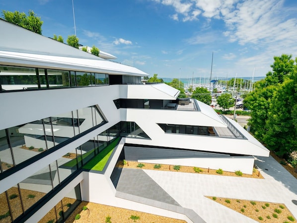 Un bâtiment moderne doté d’une façade en verre, de plusieurs étages et d’un espace paysager agrémenté d’arbres et d’arbustes.