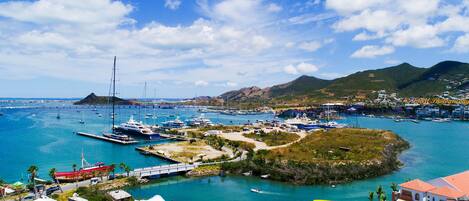 Una marina costera con barcos, un puente y un paisaje montañoso al fondo.