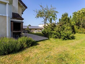 Propiedad residencial con entrada pavimentada, césped y un pequeño jardín con diversas plantas.
