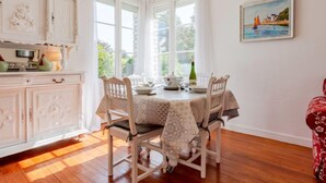 A dining area with a round table, white chairs, and a view of the outdoors through large windows.