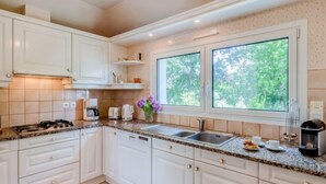 Une cuisine moderne avec des meubles blancs, un plan de travail en granit, une cuisinière à gaz, une machine à café, un grille-pain, un évier et une fenêtre donnant sur un paysage verdoyant.