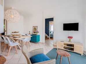 Una sala de estar moderna con comedor, un televisor montado en la pared y una escalera que sube a otra habitación.