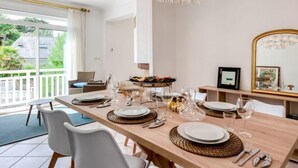 Un coin repas avec une longue table dressée pour quatre personnes, un lustre et une vue sur l’extérieur.
