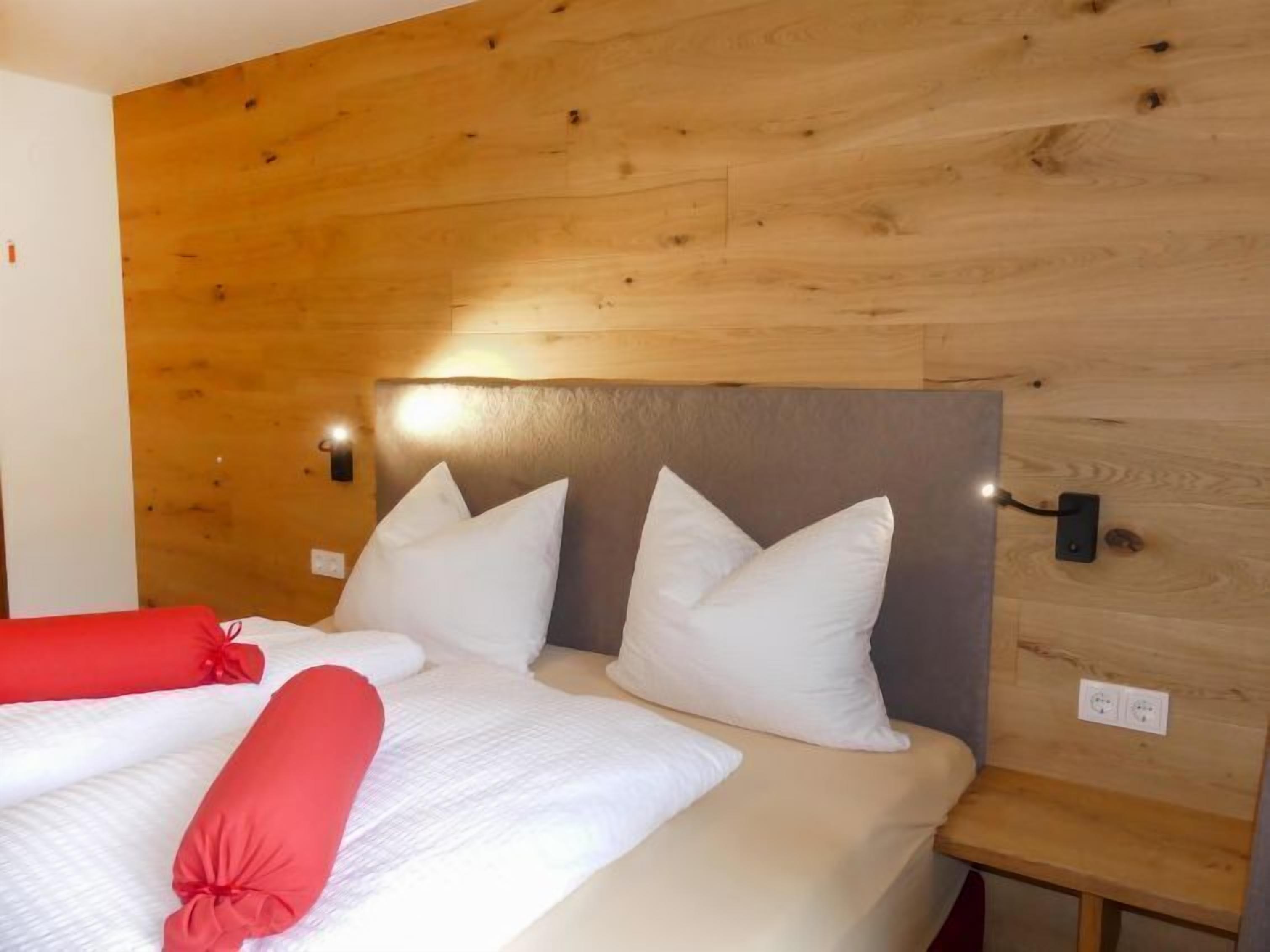 Une chambre avec une tête de lit en bois, deux lits avec une literie blanche et rouge, et une petite table de chevet.