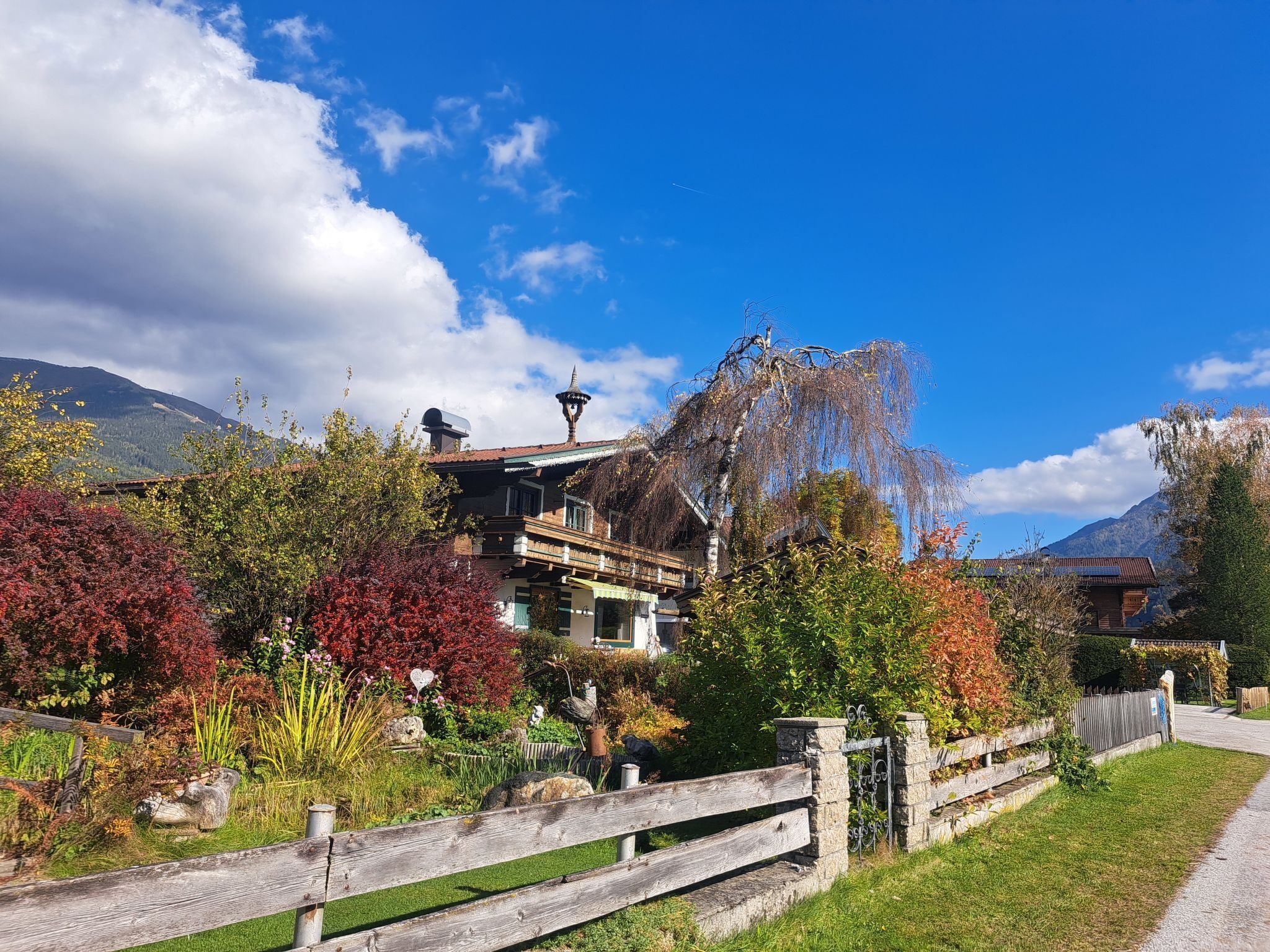 A traditional chalet with a wooden facade, a stone entrance, and a garden with autumn foliage.