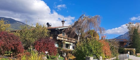 Un chalet traditionnel avec une façade en bois, une entrée en pierre et un jardin aux couleurs automnales.