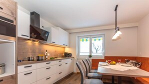 A modern kitchen with white cabinets, a wooden countertop, and a dining area with a table and chairs. - Wildkogel by Interhome (Neukirchen am Großvenediger)