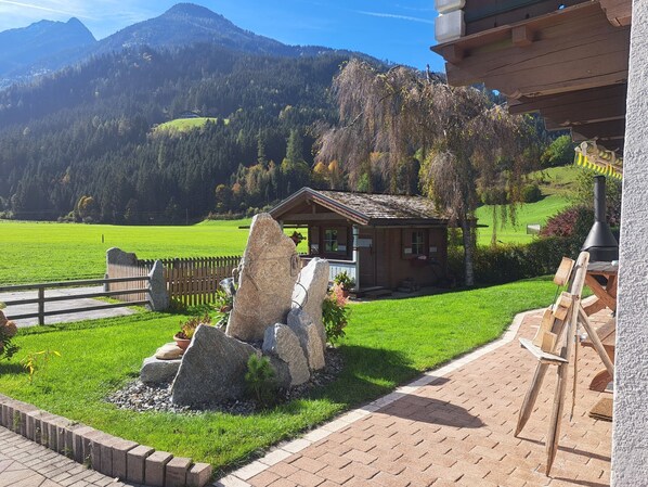 A rustic cabin with a stone waterfall feature, surrounded by a well-maintained lawn and a wooden fence.
