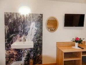 A bathroom with a sink, a mirror, a television, and a wooden vanity with a vase of flowers.