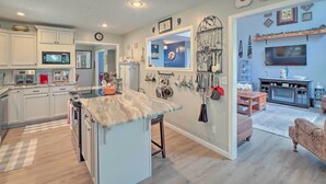 A modern kitchen with white cabinets, a marble countertop, and a large island. There are hanging pots and pans on the wall, and a TV mounted above the counter. - 10-Acre Mountain Home Getaway w/ Fire Pit (Mountain Home)
