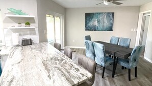 A modern kitchen with a marble countertop, a dining area with a dark wooden table and blue chairs, and a ceiling fan. - DOLPHIN HOUSE. 7 min drive to the Beach! (Seminole)