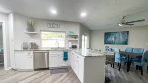 A modern kitchen with white cabinetry, a marble island, and a dining area with blue chairs. - DOLPHIN HOUSE. 7 min drive to the Beach! (Seminole)