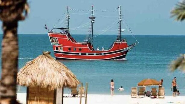 A beach with a red boat in the water, a thatched-roof hut, and beach chairs. - DOLPHIN HOUSE. 7 min drive to the Beach! (Seminole)