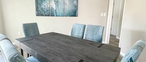 A dining room with a dark wooden table and matching chairs, a large abstract painting on the wall, and a door leading to another room.