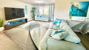 A living room with a large flat-screen TV, a grey sofa, a patterned rug, and a painting of a whale. - DOLPHIN HOUSE. 7 min drive to the Beach! (Seminole)