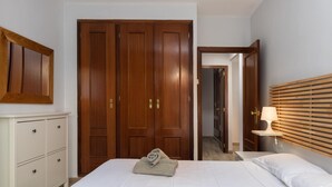 A hotel room with a bed, a wooden wardrobe, a bedside table with a lamp, and a mirror on the wall.